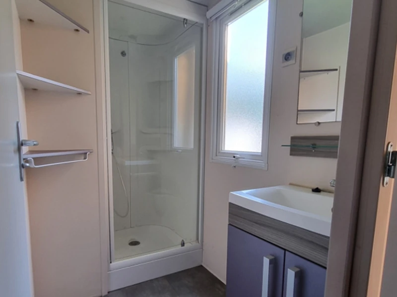 Salle de bain spacieuse et lumineuse dans un mobil-home. Lavabo avec rangement et cabine de douche
