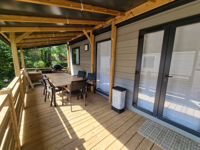 Grande terrasse bois couverte d'un mobil-home avec une grande table et 6 chaises