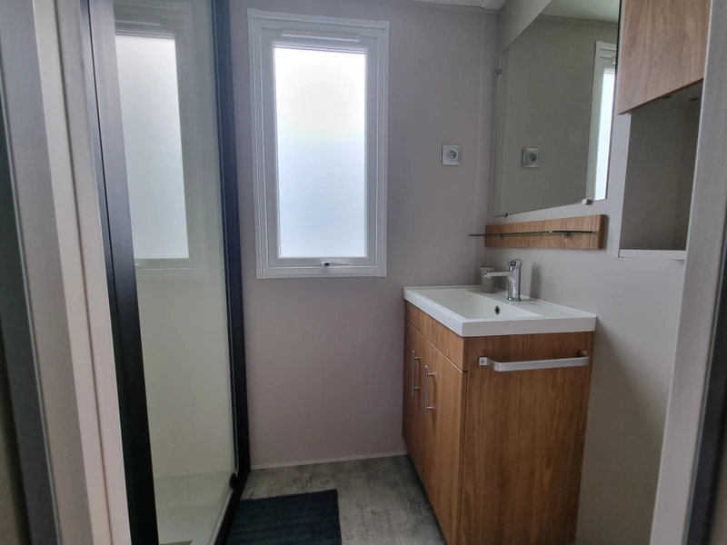 Salle de bain d'un mobil-home avec douche, lavabo et rangements