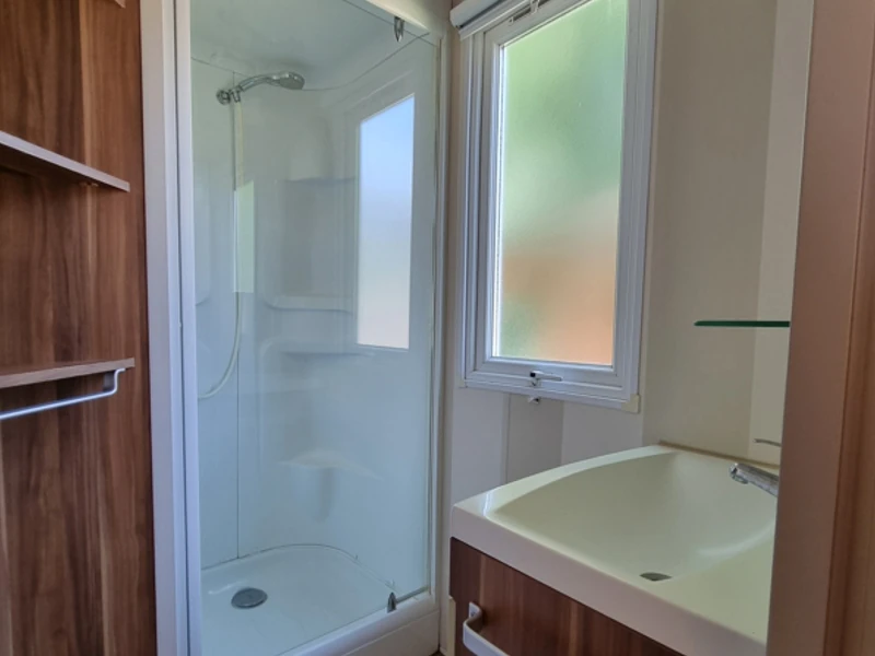 Salle de bain avec douche, lavabo et rangements d'un mobil-home en Savoie