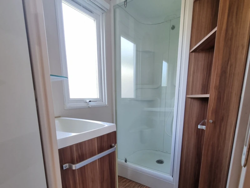 Salle de bain d'un mobil-home avec cabine de douche, lavabo et rangements
