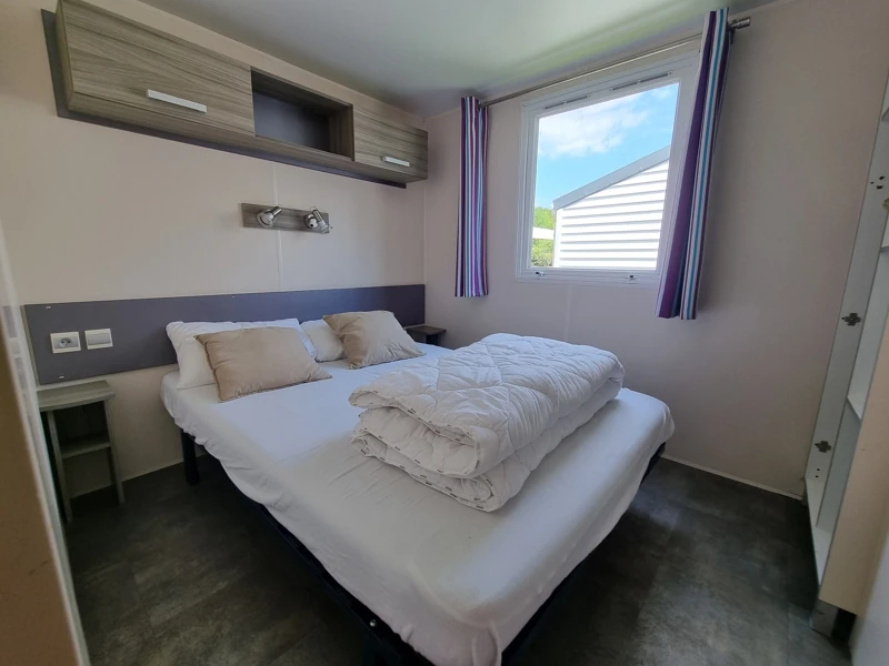 Chambre parentale dans un mobil-home avec une belle fenêtre et des rangements