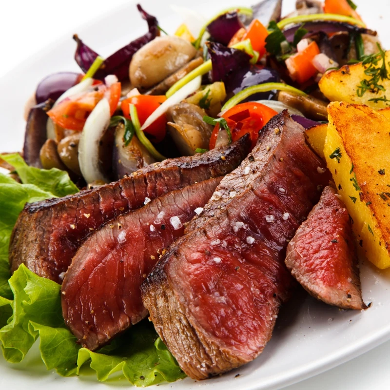 Une assiette avec une viande grillée et tranchée accompagnée de pommes de terre rôties et petits légumes d'été
