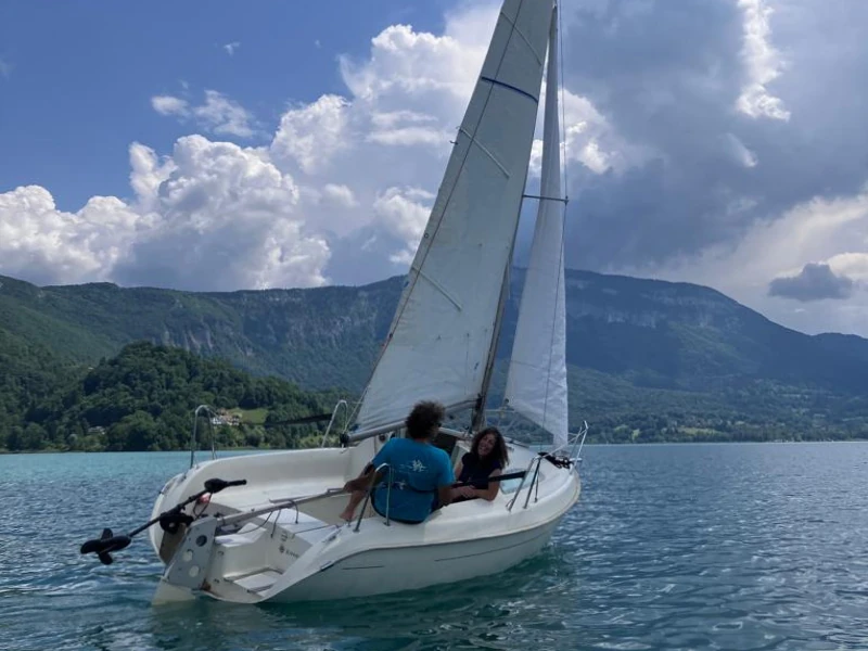 Un homme et une femme sont à bord d'un petit voilier qui navigue sur le lac d'Aiguebelette