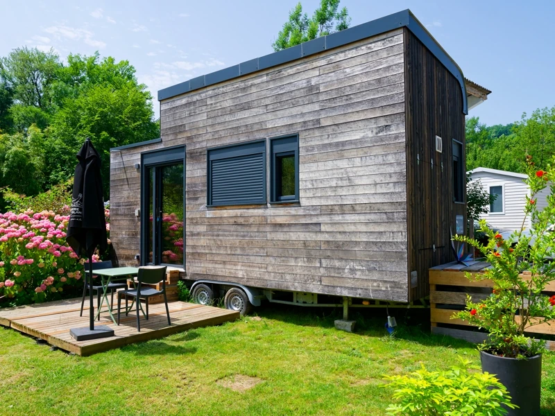 Tiny-house en bois avec petite terrasse et salon de jardin sur un emplacement verdoyant et fleuri