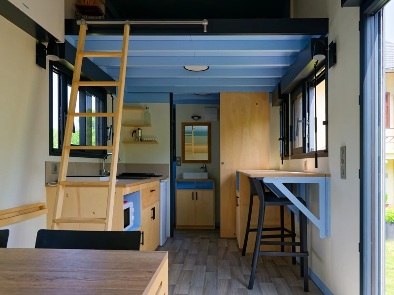 Vue intérieure d'une tiny house avec salle de bain, cuisine équipée et espace repas au rez de chaussée et chambre en mezzanine