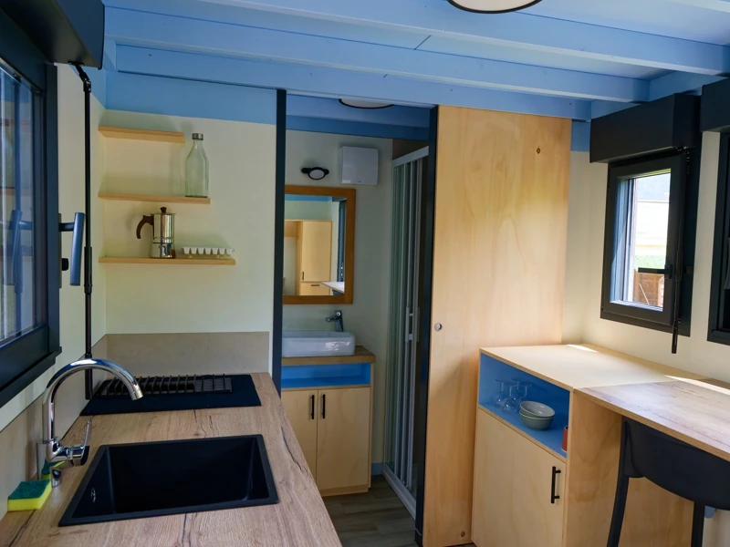 Vue intérieure d'une tiny house avec salle de bain, cuisine équipée et espace repas