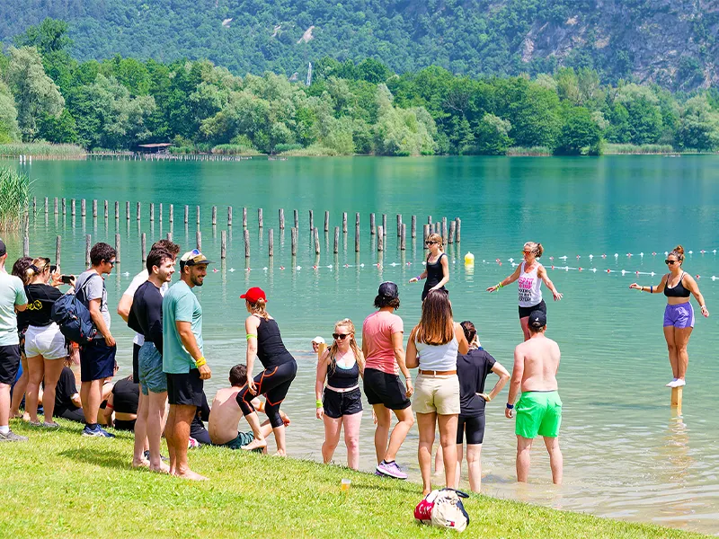 Un groupe de personnes s'amuse au bord du lac. Ils jouent à Koh Lanta juchés sur des poteaux en bois plantés dans le l'eau.